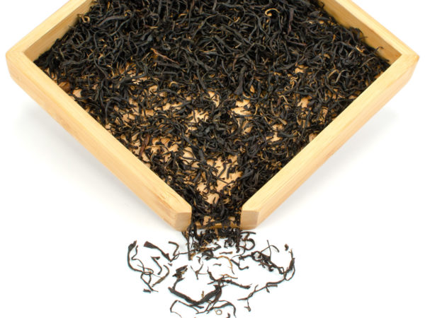 Qimen Caixia (Sunrise Keemun) dry black tea leaves displayed on a bamboo tray.