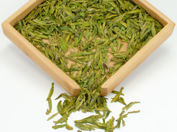Shifeng Longjing (Shifeng Dragon Well) dry green tea leaves displayed on a bamboo tray.