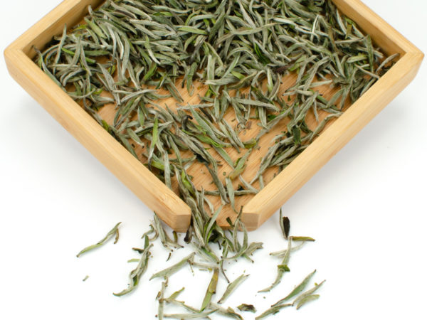 Baihao Yinzhen (Silver Needle) dry white tea leaves displayed on a bamboo tray.